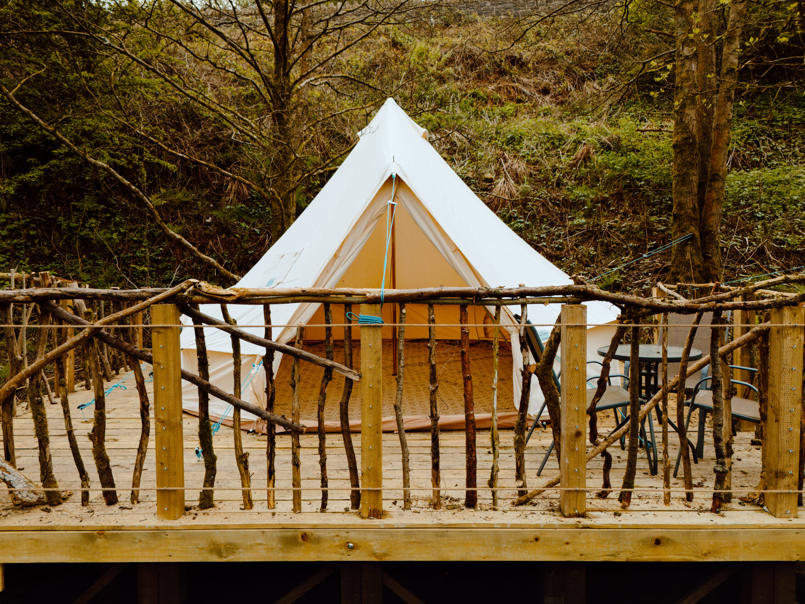A white bell tent on a wood deck surrounded by a wood fence made of tree branches